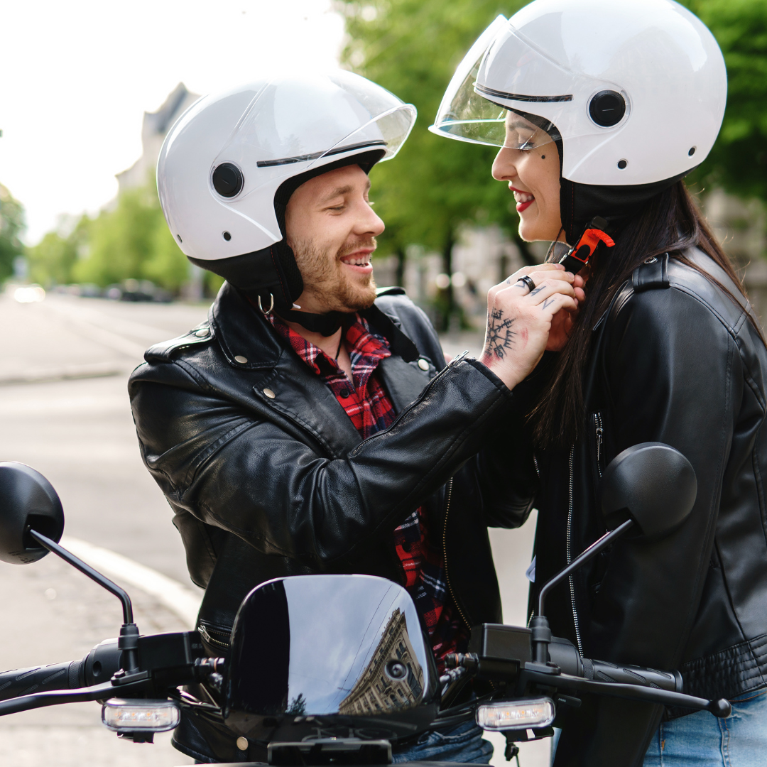 A man and woman enjoying a motorcycle date, both dressed in stylish outfits and wearing helmets.